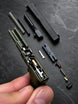 A close-up of a hand holding an olive green Die-Cast Keychain frame with its internal components exposed, surrounded by disassembled parts on a dark textured surface.