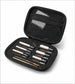 An open black zippered carrying case containing multiple cleaning and inspection tools, including white and gold-handled brushes and metal pins, photographed on a light gray background.