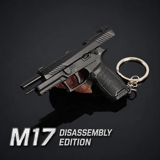 A black pistol-shaped keychain with a metal key ring and split ring, shown on a dark reflective background with the text 'M17 DISASSEMBLY EDITION' at the bottom left.