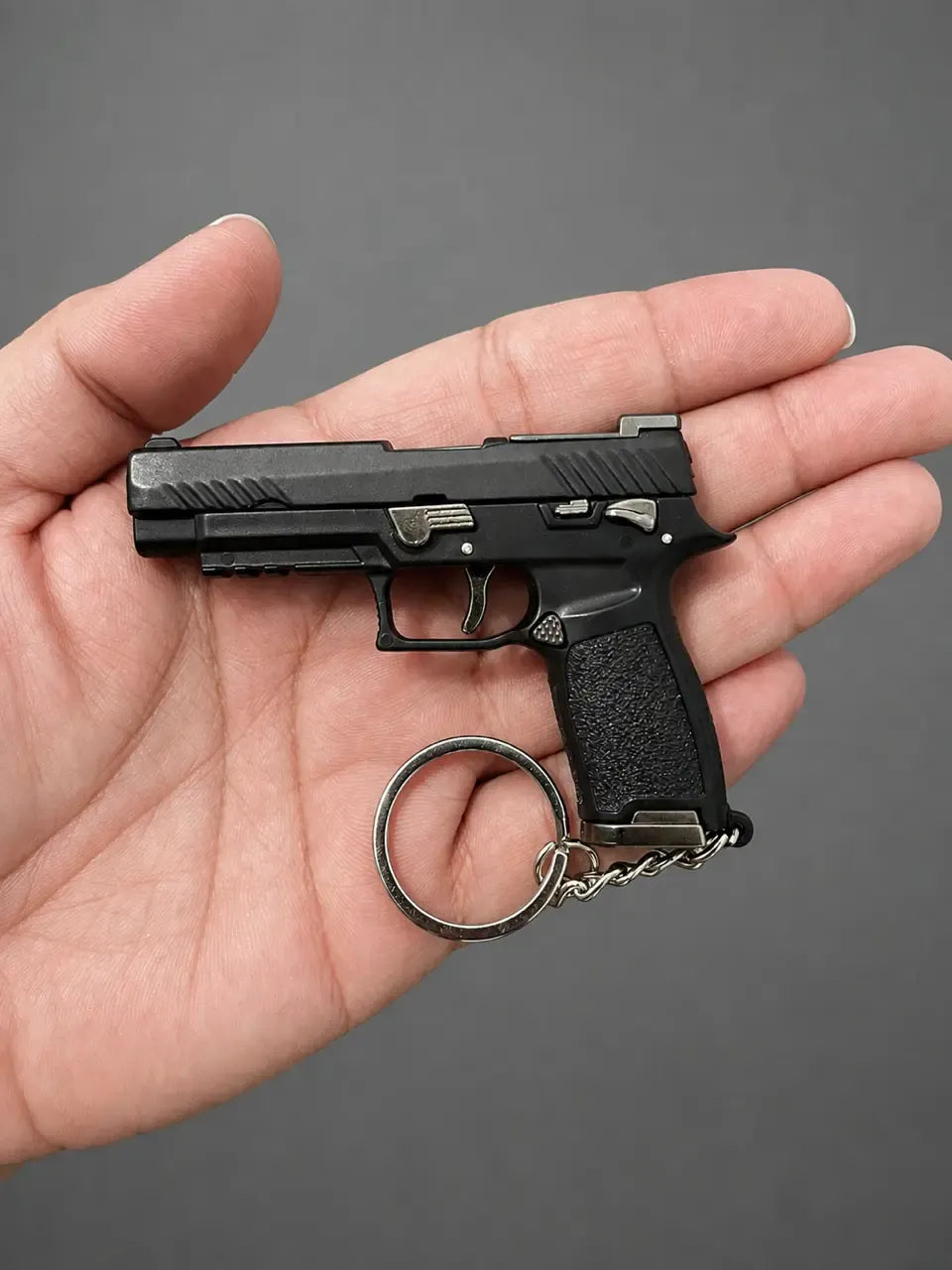 A miniature black handgun-shaped keychain held in a person's hand against a plain gray background.