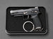 A black semi-automatic pistol keychain displayed inside a black rectangular presentation box with a textured foam insert, set against a dark gray background.