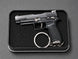 A black semi-automatic pistol keychain displayed inside a black rectangular presentation box with a textured foam insert, set against a dark gray background.