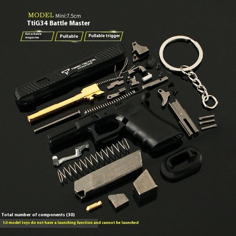 A 1:13 scale model TTi G34 Battle Master miniature keychain kit, shown in a disassembled state with its various components neatly arranged on a dark reflective surface. The kit includes a black keychain body, a gold-colored barrel, a black textured carrying case, a silver metal keychain, springs, screws, and other mechanical parts.