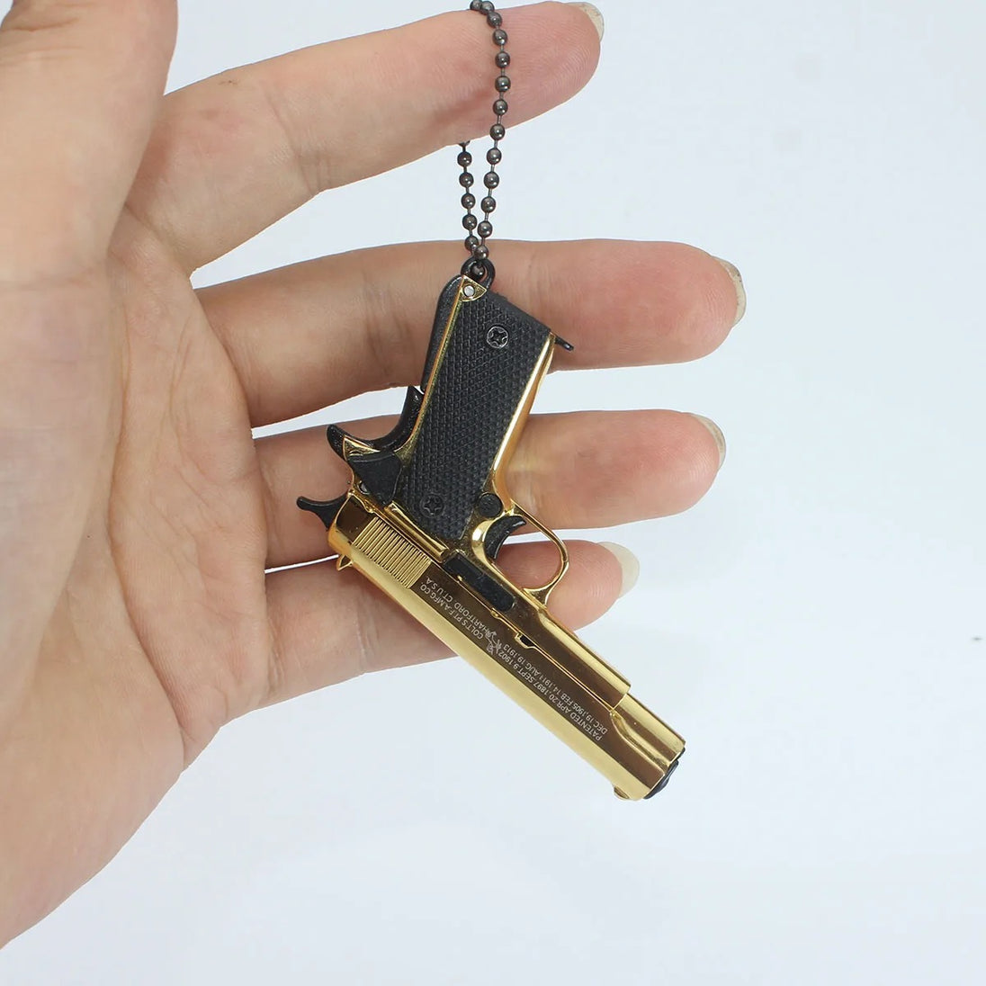 1:3 1911 Scale Handgun - Gold miniature with black grips held in hand on keychain against white background
