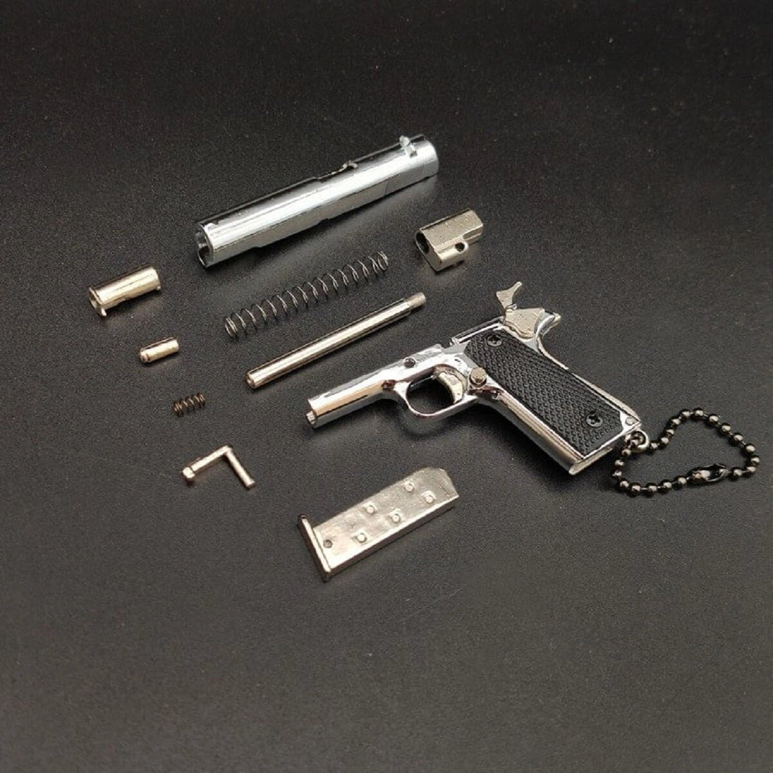1:3 1911 Scale Handgun - Silver miniature die cast metal model with disassembled parts on black background.