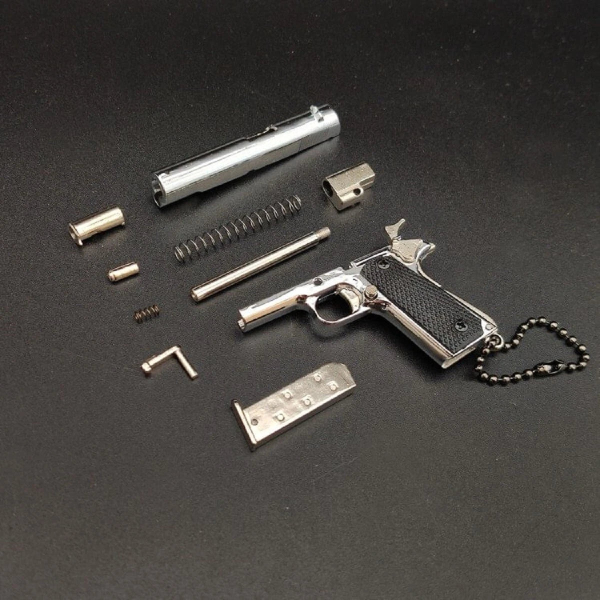 1:3 1911 Scale Handgun - Silver miniature die cast metal model with disassembled parts on black background.